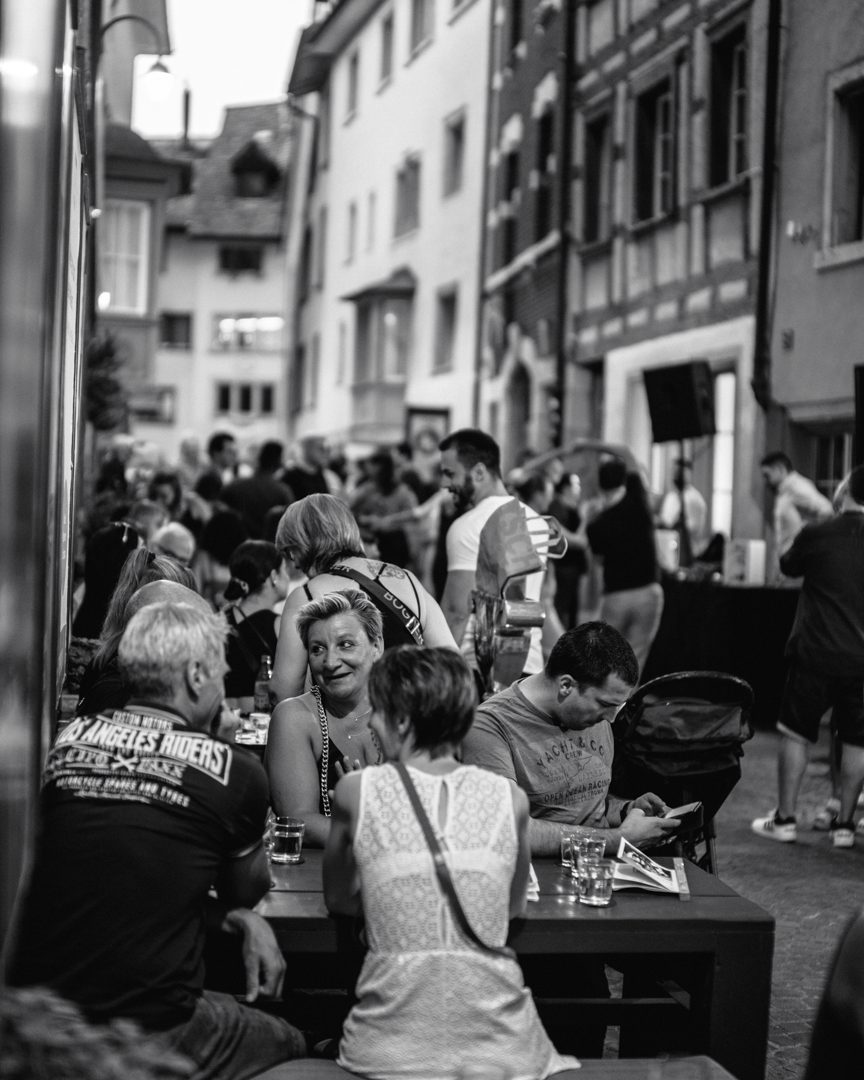 Belebte Gasse voller Gäste an Bartischen an einem lauen Abend